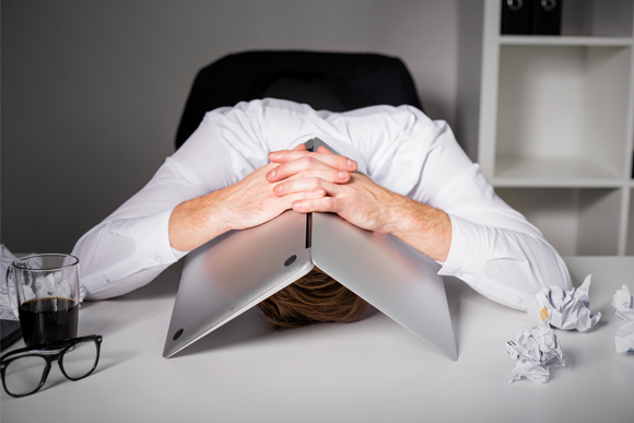 Man with head under laptop, frustrated